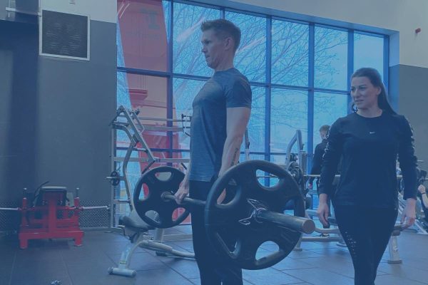 A personal trainer training her client to do deadlifts in a gym